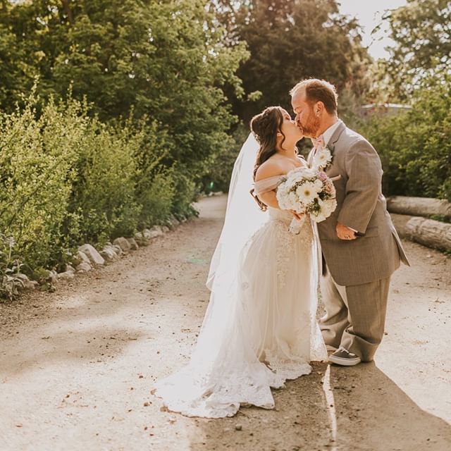 Bride Wearing A White Wedding Dress Holding Bouquet Next To Groom In Gray Suit.