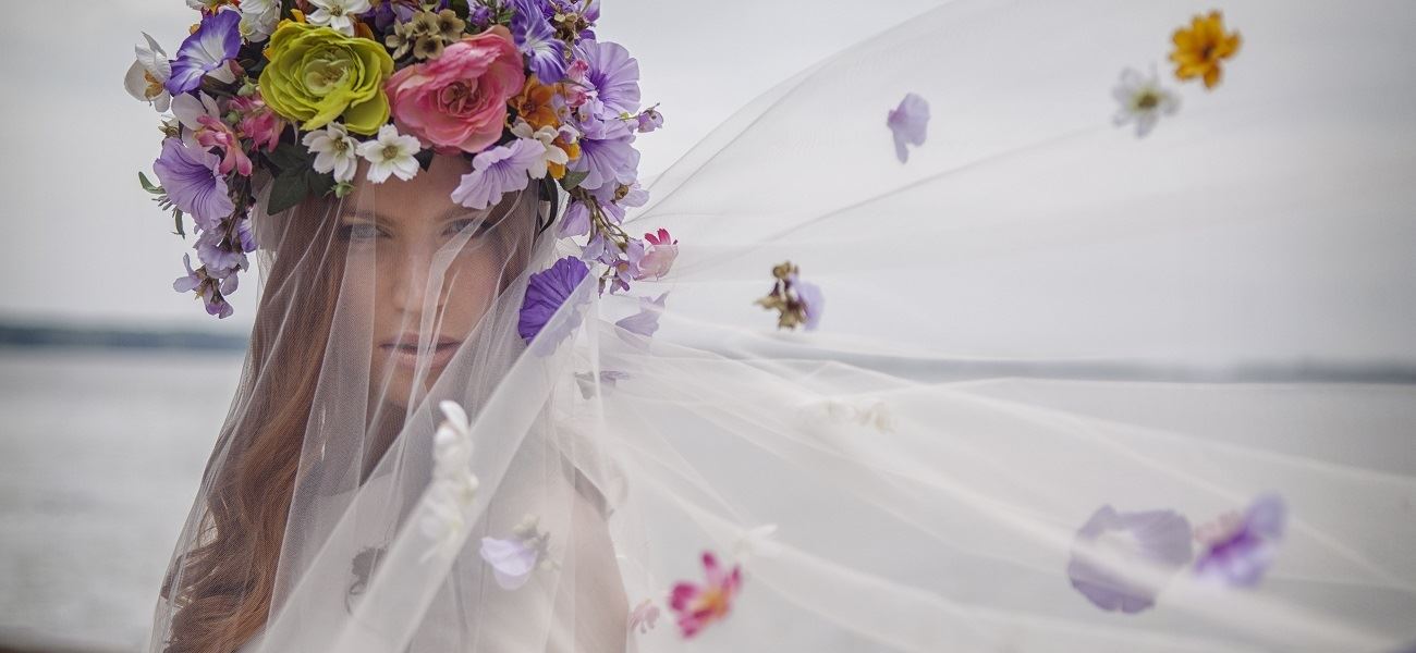 Bride Wearing A Large Flower Crown Featuring Purple And Pink Flowers. Veil Is Under The Flower Crown.