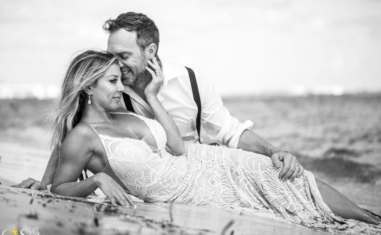 Black And White Photo Of Bride And Groom Laying On Sand At The Beach.