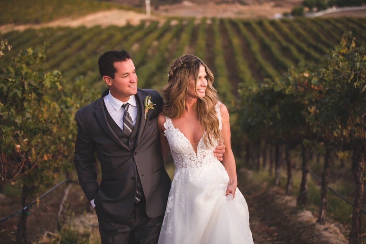 Bride And Groom Walking Through Vineyard
