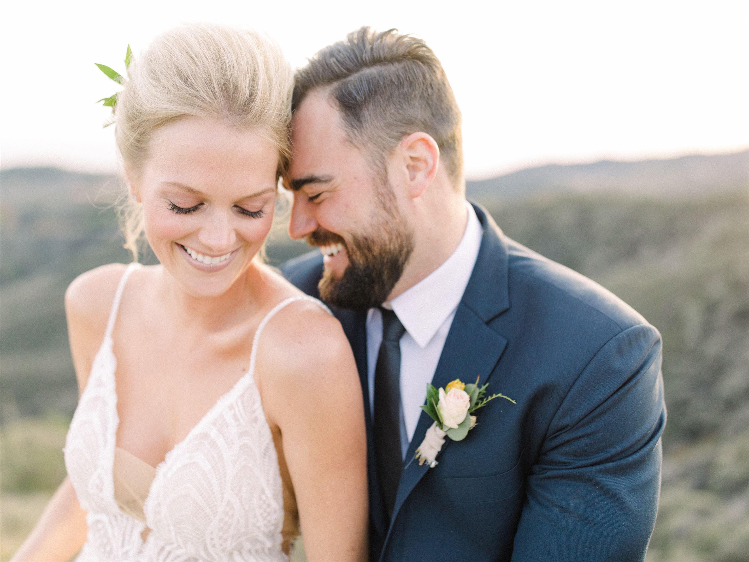 Blonde Bride Wearing A White Wedding Dress Sitting Next To Groom In Tux.
