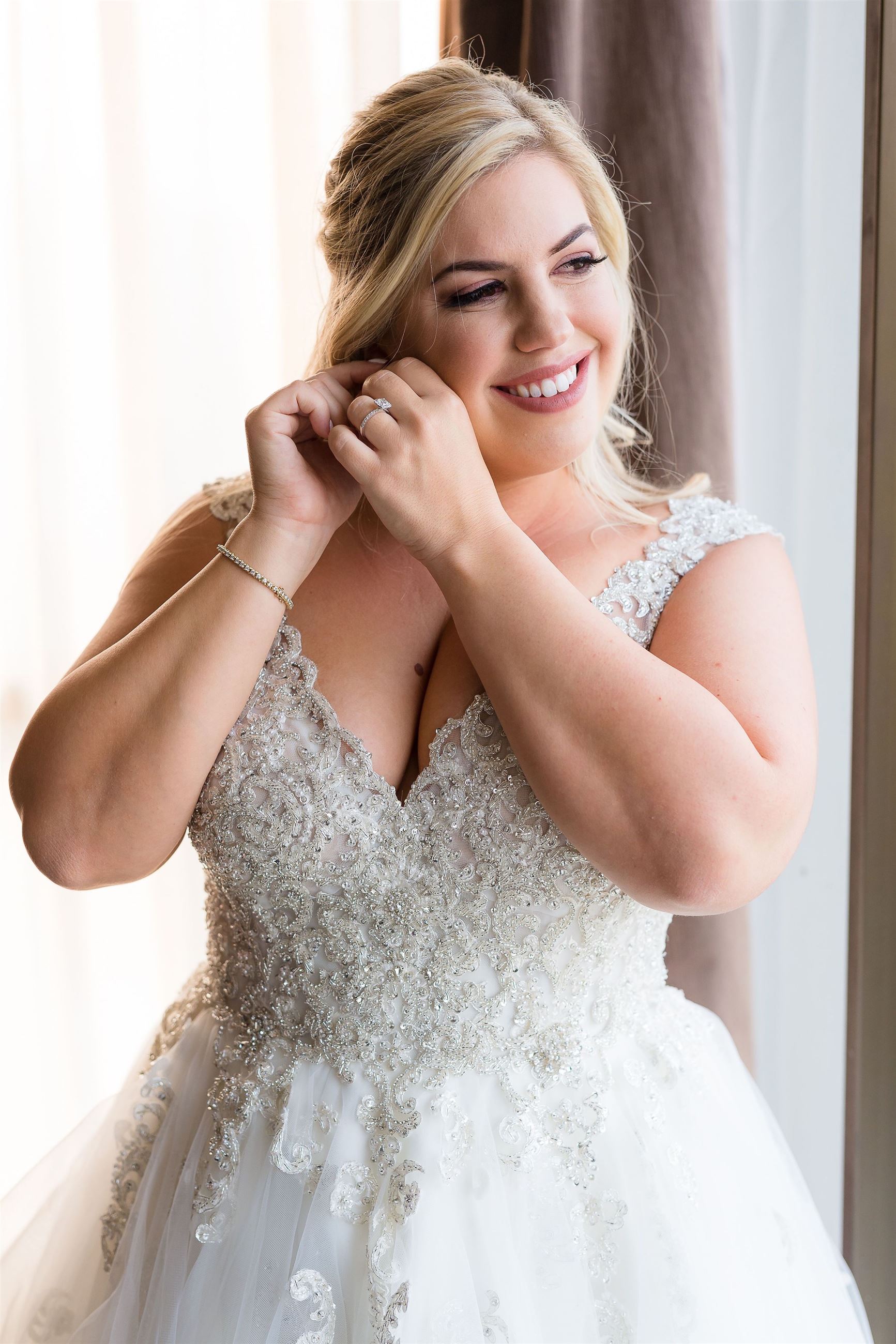 Plus Size Bride Wearing A White Wedding Dress And Putting On Earrings.