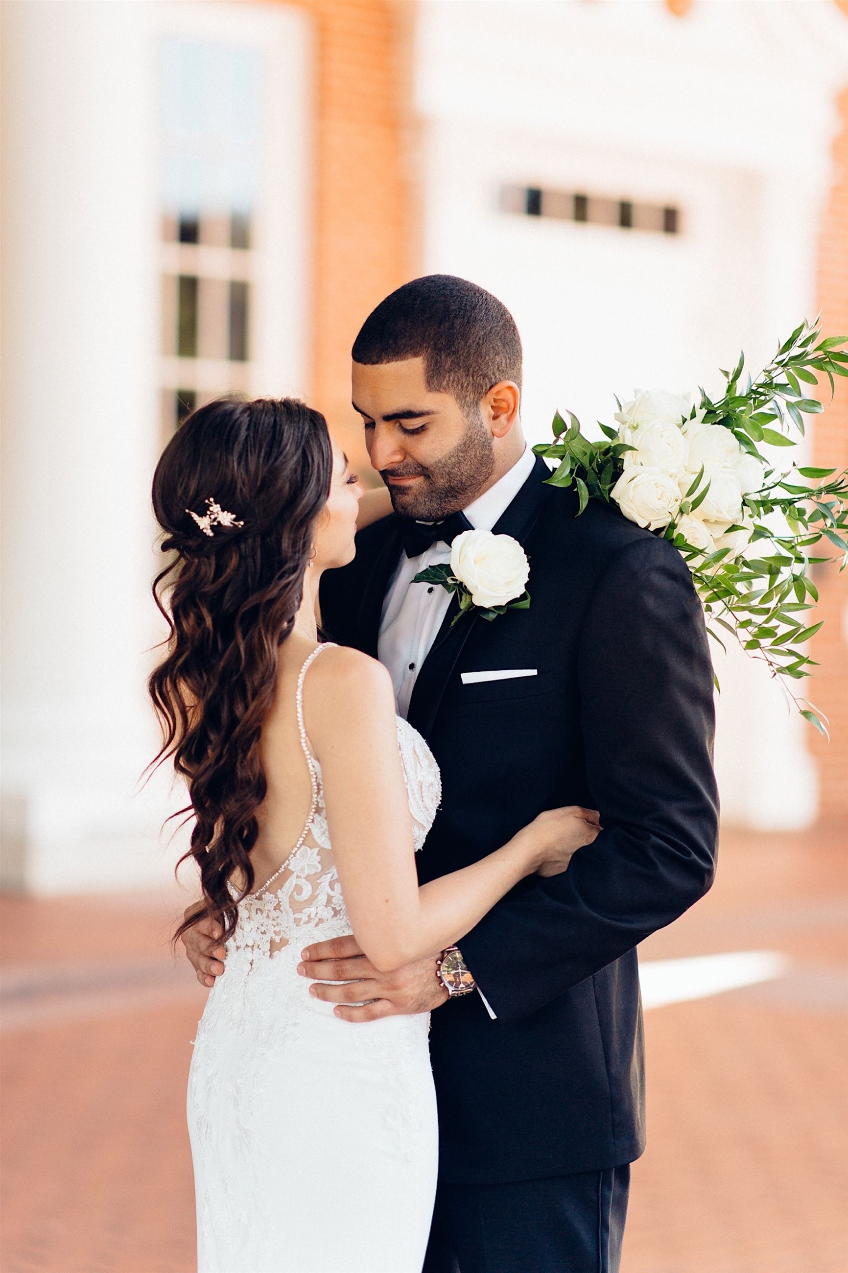 Bride Wearing A White Wedding Dress And Hugging Groom In Black Tux