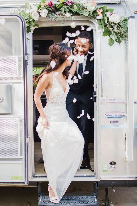 Bride walking out of an airstream van wearing a tight wedding dress. Groom is following her out of the van.