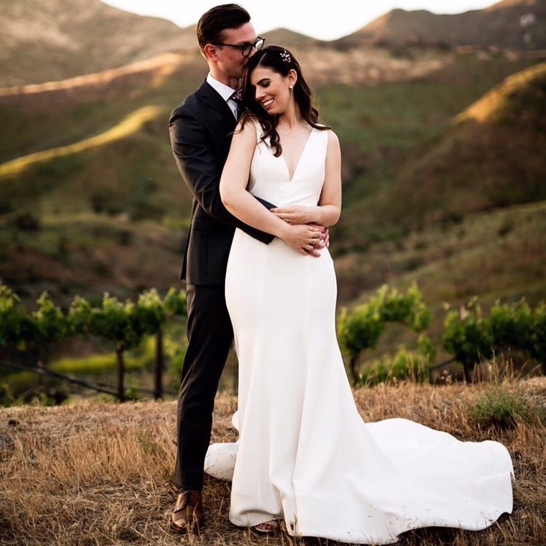 Bride Wearing White Simple Wedding Dress Standing In Front Of Groom.