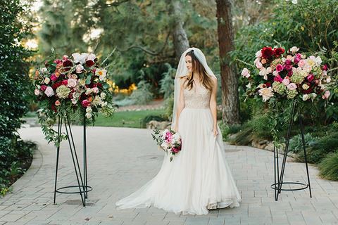 Bride wearing an a-line wedding dress and a veil. Bride is standing between two flower planters.
