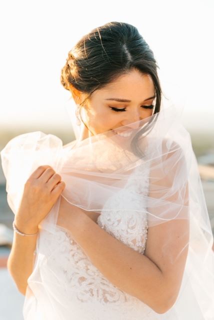 Brunette Bride Wearing A White Wedding Dress With Veil Wrapped Around Her.