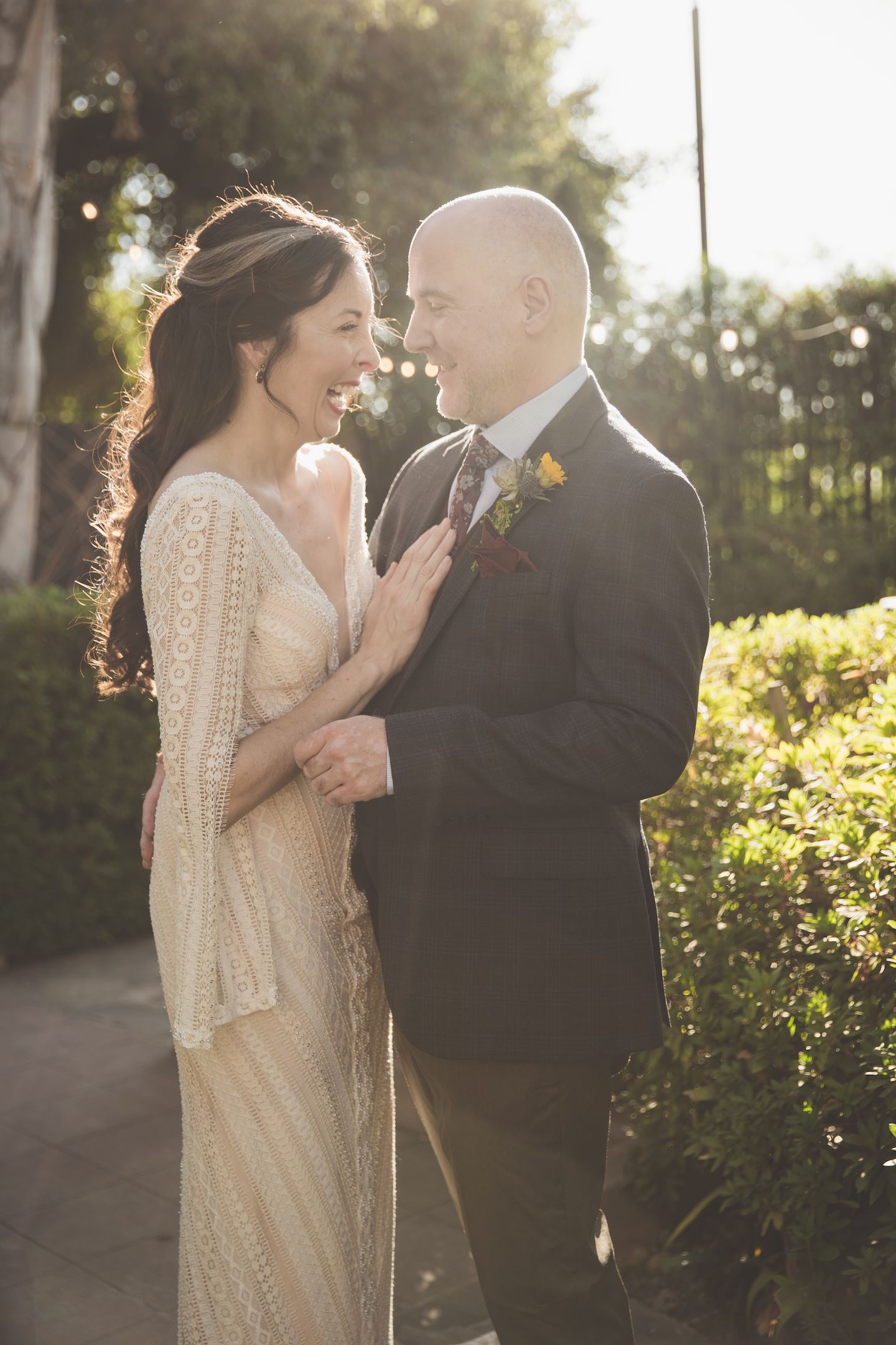 Bride And Groom Standing In Front Of Bush Laughing.